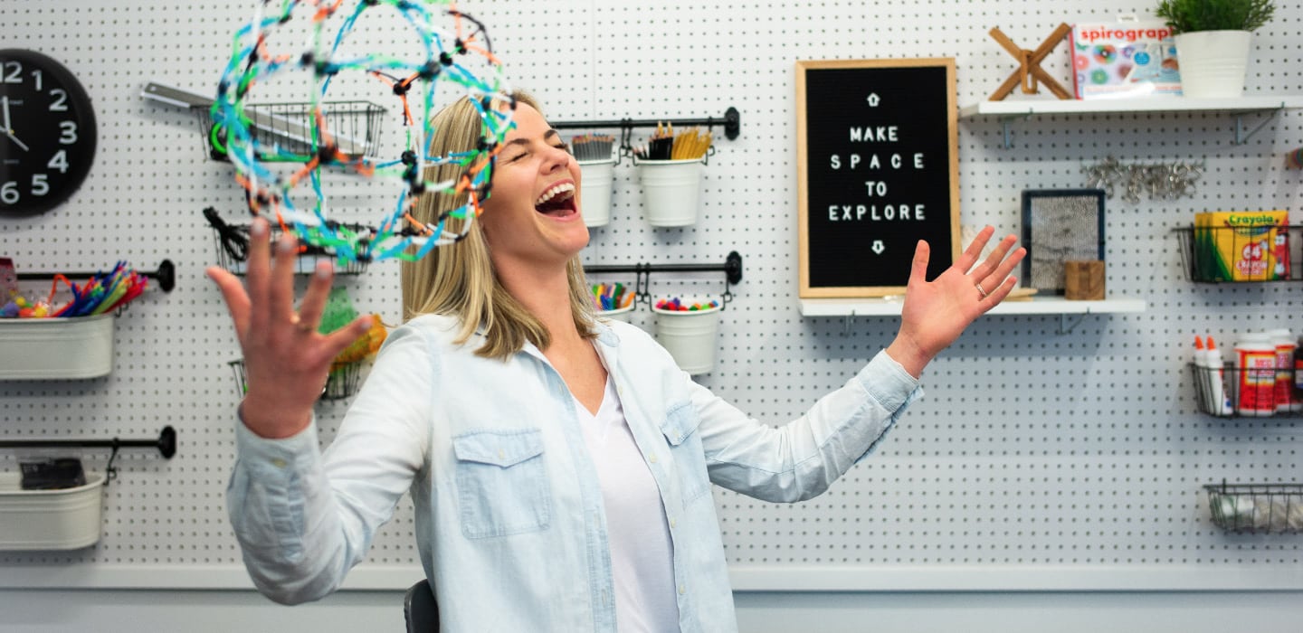 Laughing woman playing with a Hoberman sphere in a maker space.